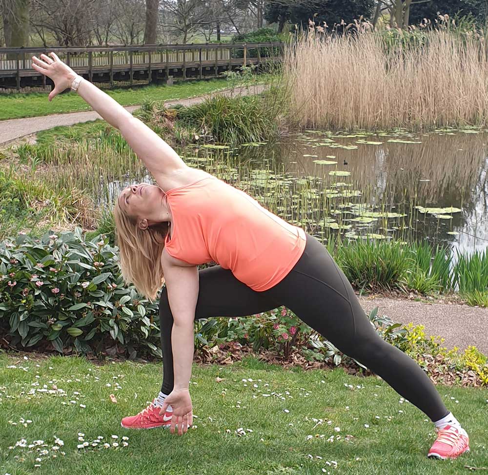 Urska Wall in gym clothing doing a yoga stretch in a park in front of a pond